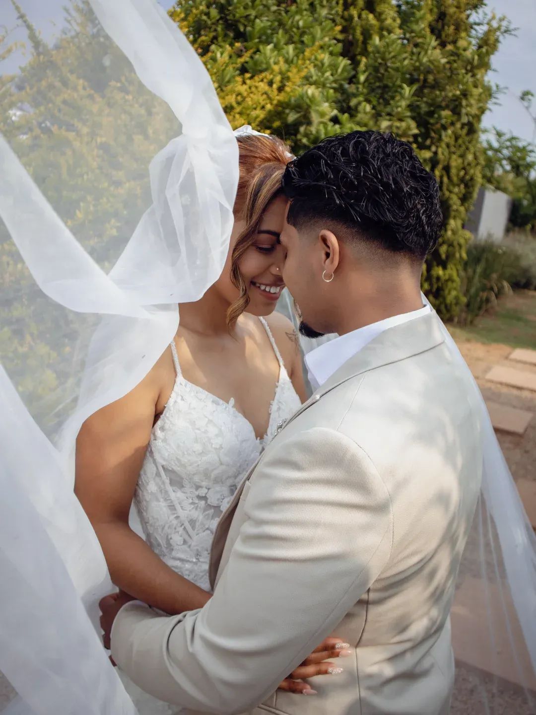 Bride and groom embracing under a flowing veil in the garden