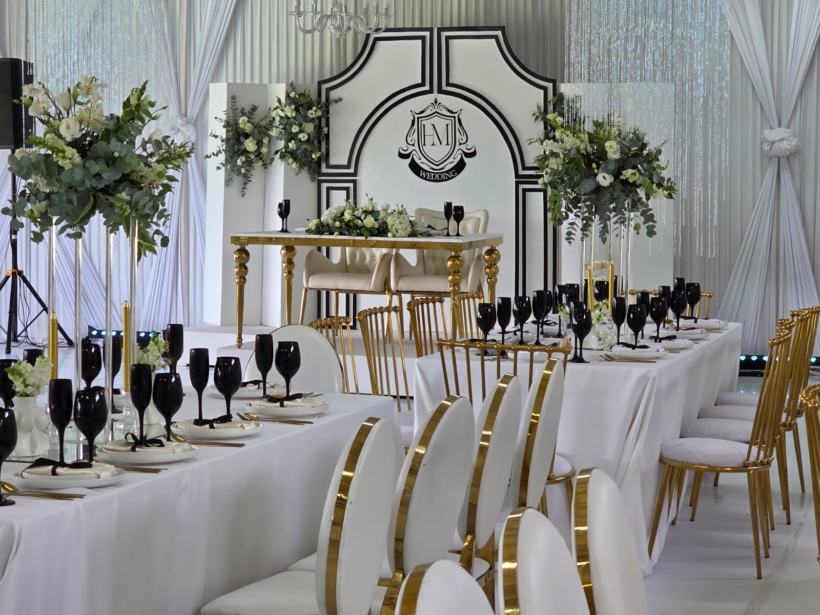 Elegant wedding reception sweetheart table with gold chairs, floral arrangements and chandeliers
