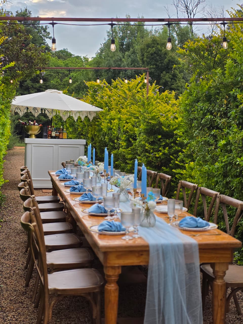 Styled outdoor dining table with blue napkins, candles and fairy lights in the Muano garden